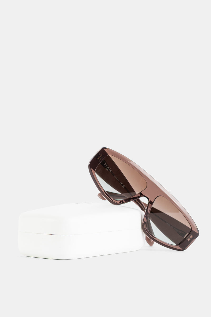 Maison Alaïa lunettes Azzedine posées sur écrin blanc, profil acétate brun et verres dégradés