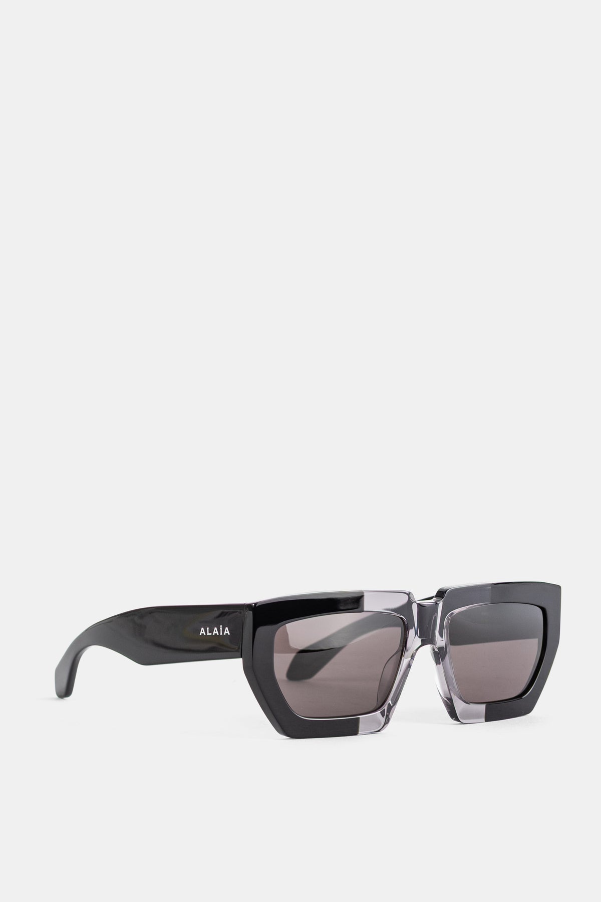 Maison Alaïa sunglasses vue trois quarts branches noires glossy contour inférieur cristal fumé collection FW26