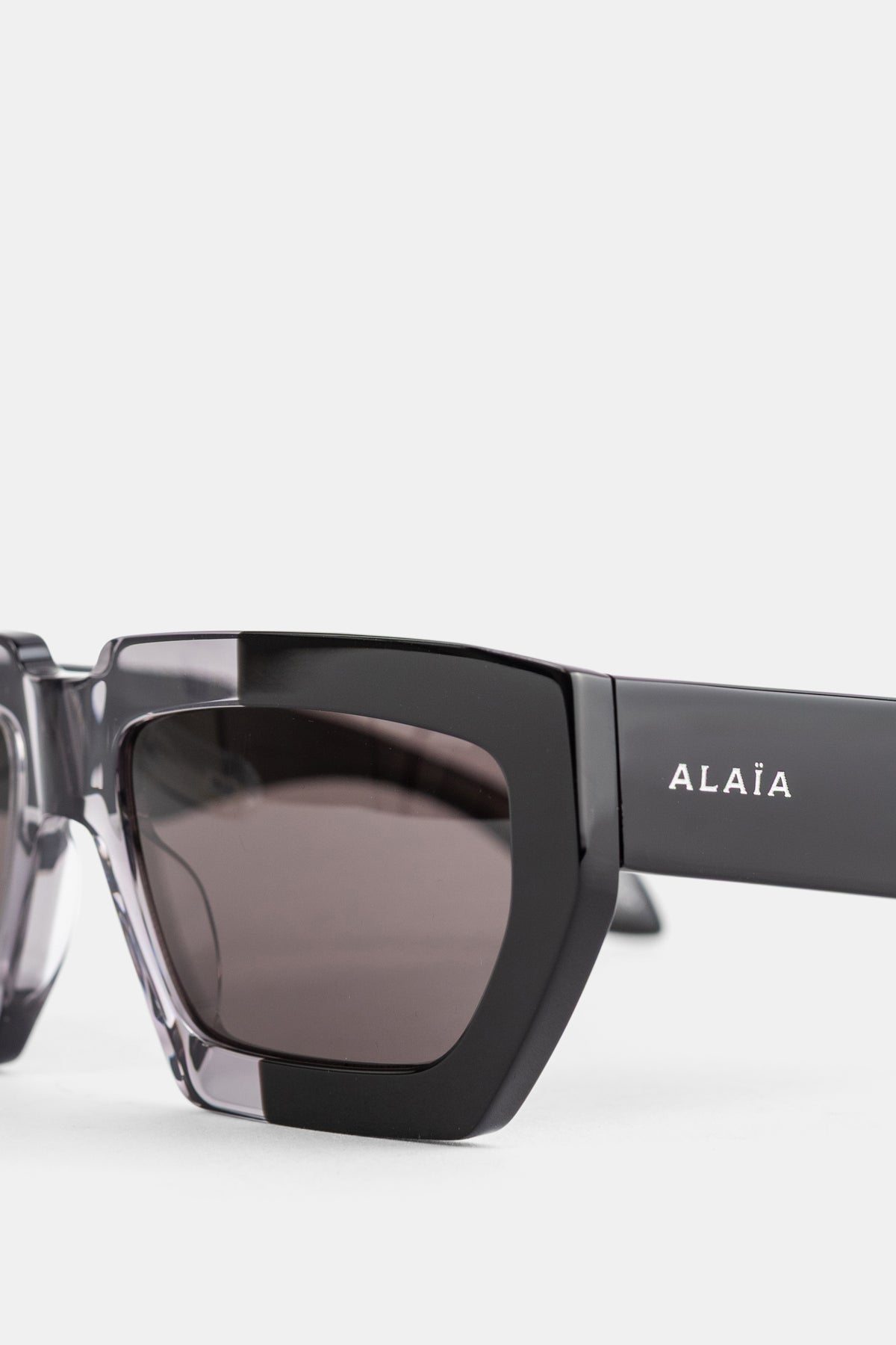 Maison Alaïa lunettes oversize gros plan branche noire logo blanc gravé verre fumé gris cat-eye FW26