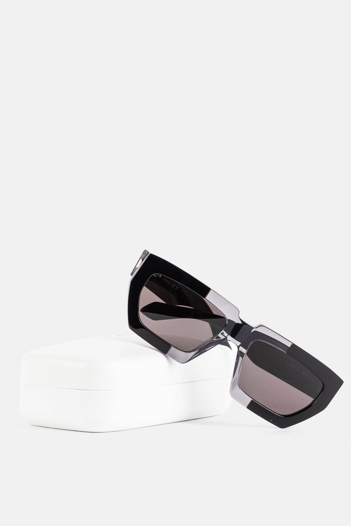 Maison Alaïa lunettes soleil posées sur étui blanc bicolore noir cristal fumé vue de profil FW26
