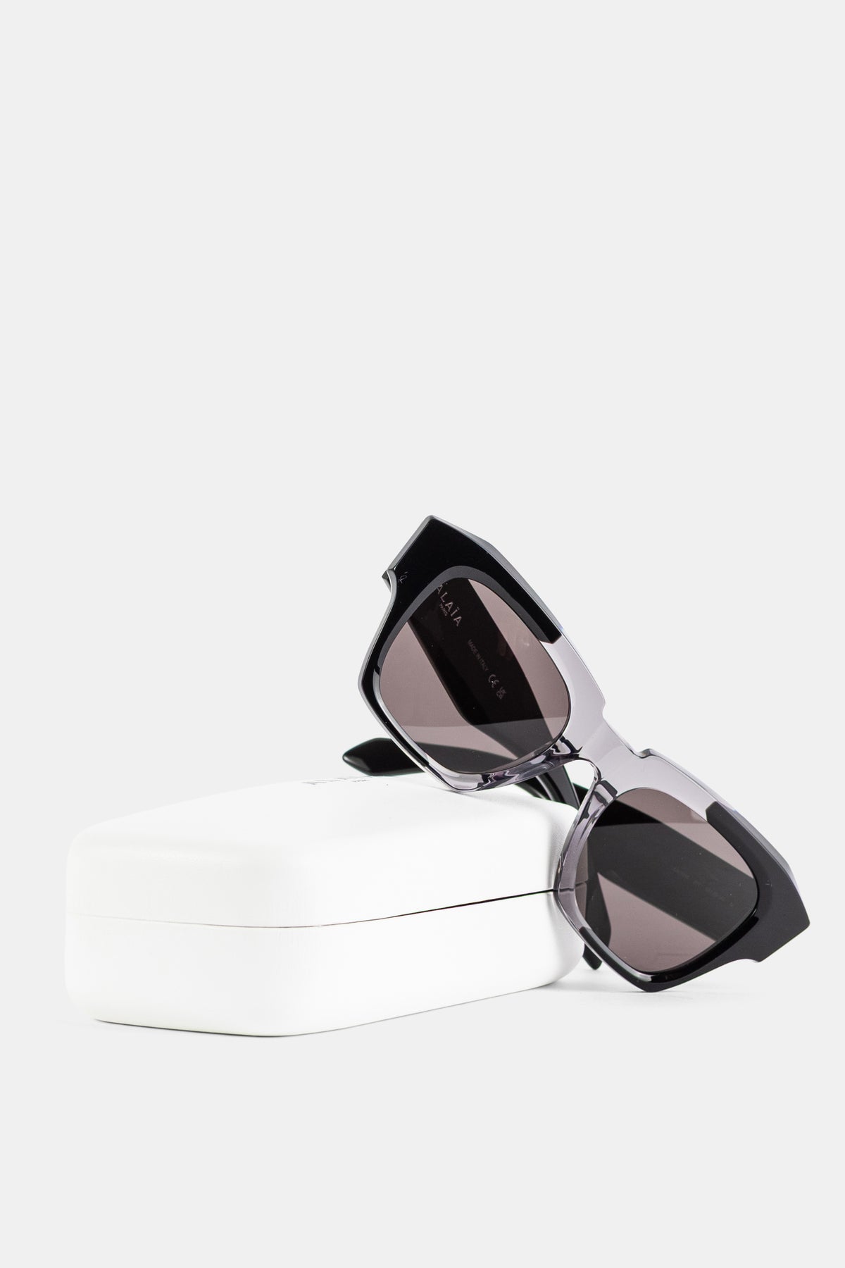 Maison Alaïa lunettes soleil carrées posées sur écrin blanc verres gris fumés monture bicolore FW26