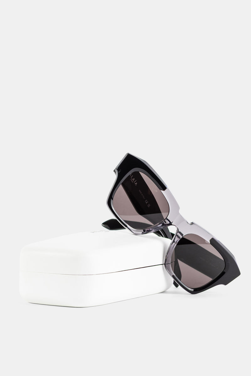 Maison Alaïa lunettes soleil carrées posées sur écrin blanc verres gris fumés monture bicolore FW26