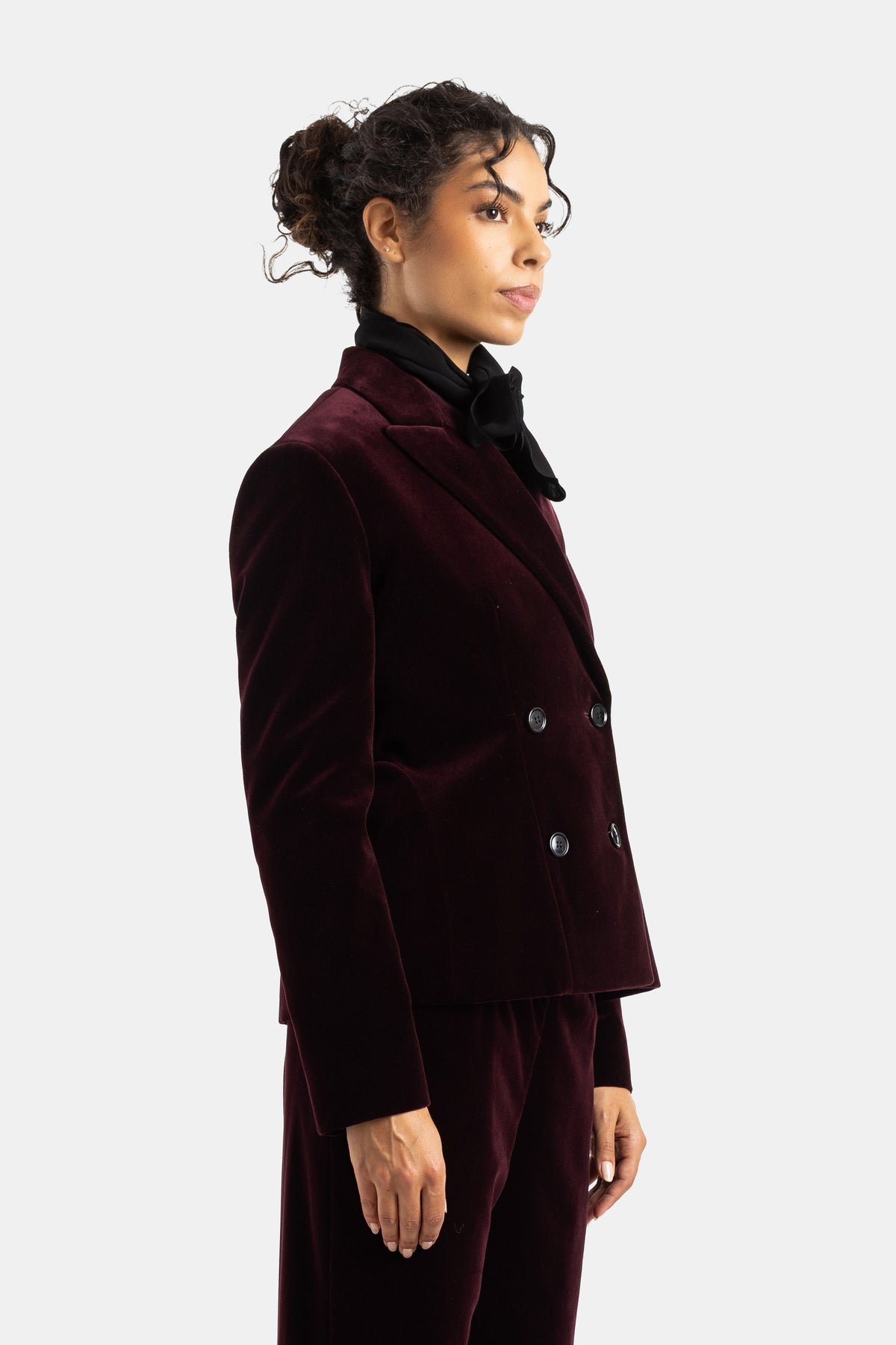 Blazer Maison Alaïa de terciopelo berenjena con doble botonadura visto de perfil y pañuelo negro anudado