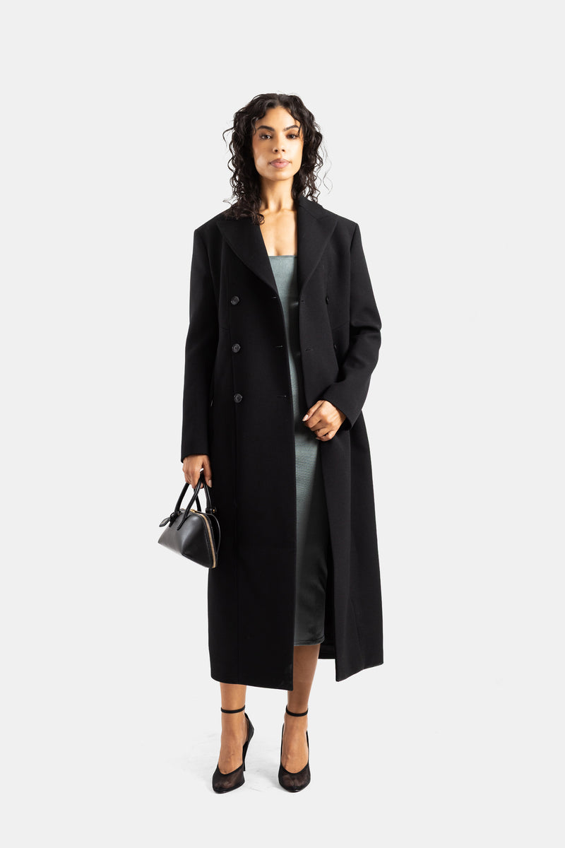 Maison Alaïa women's maxi length double-breasted black wool coat styled from the front over a slate grey midi dress.