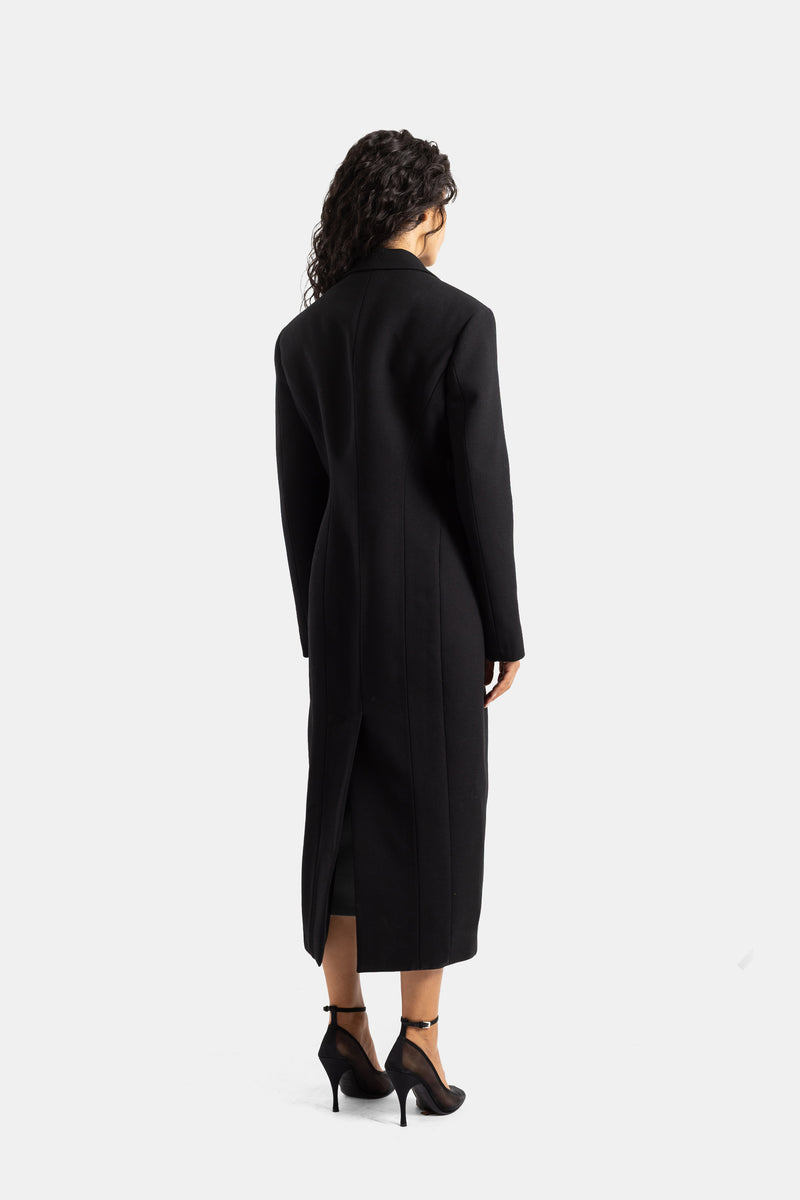 Back view of Maison Alaïa women's long black wool coat with vertical seams, structured shoulders, and back slit.