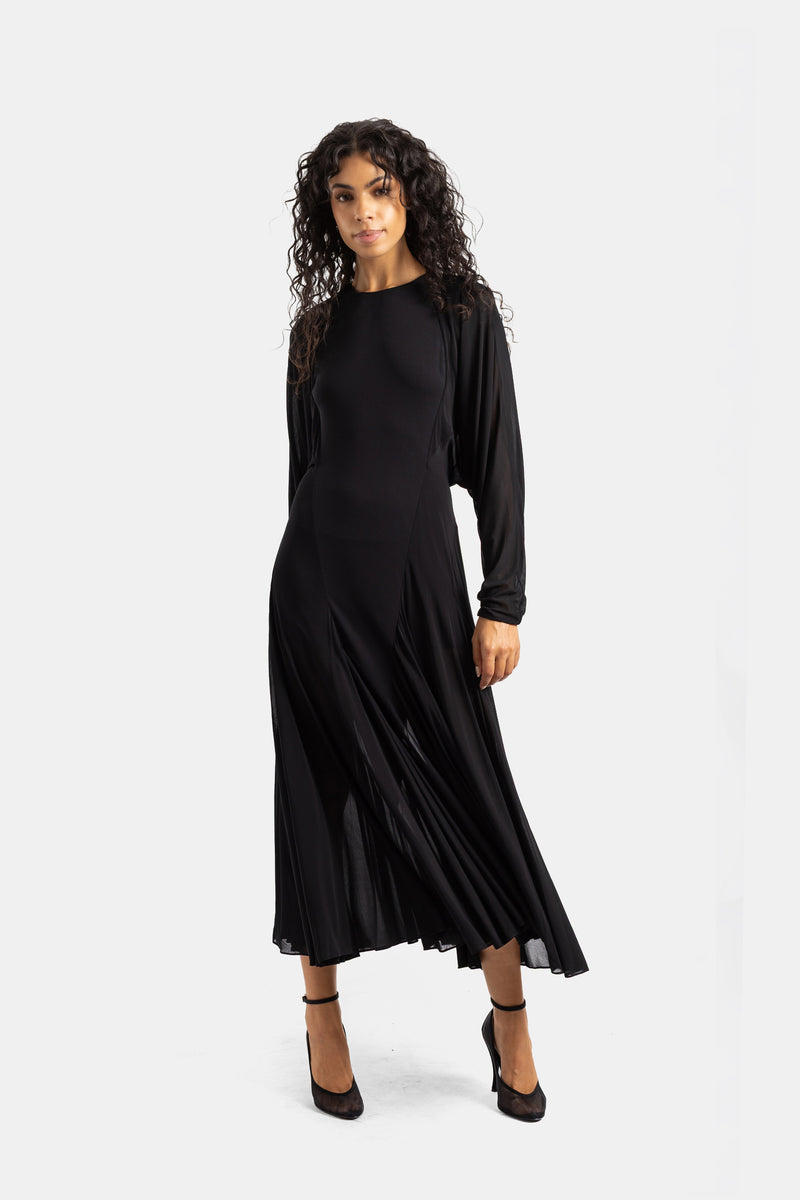 Abito midi nero Maison Alaïa indossato di fronte, con gonna a godet ondulata e maniche fluide cascanti in chiffon.