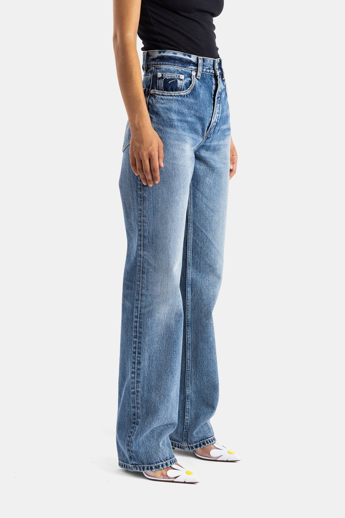 Maison Alaïa jean femme coupe droite en denim bleu lavé, vue de profil avec chaussures fleuries