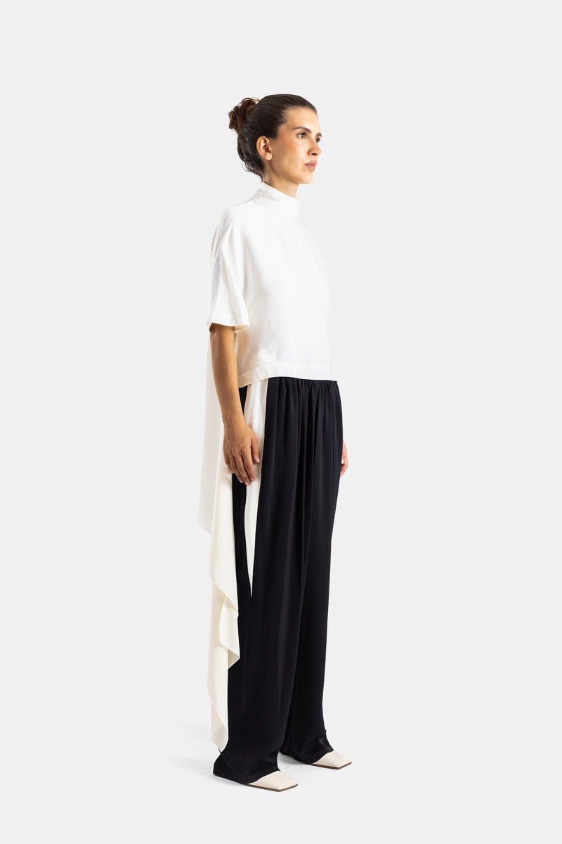 Maison Alaïa top crème pan drapé tombant vue profil, contraste avec pantalon fluide noir et escarpins blancs