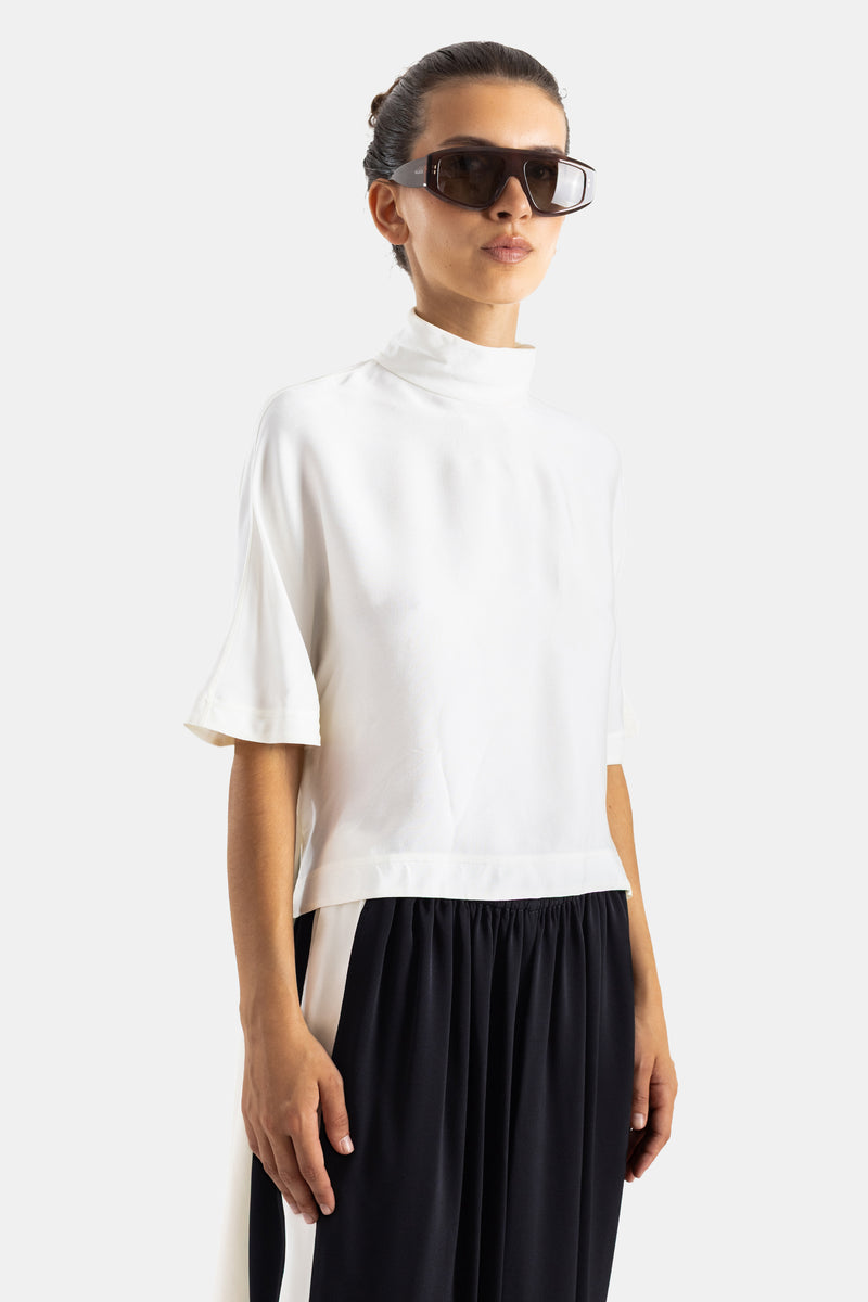 Maison Alaïa top col cheminée crème porté de trois-quarts, manches évasées viscose satinée, lunettes de soleil oversize