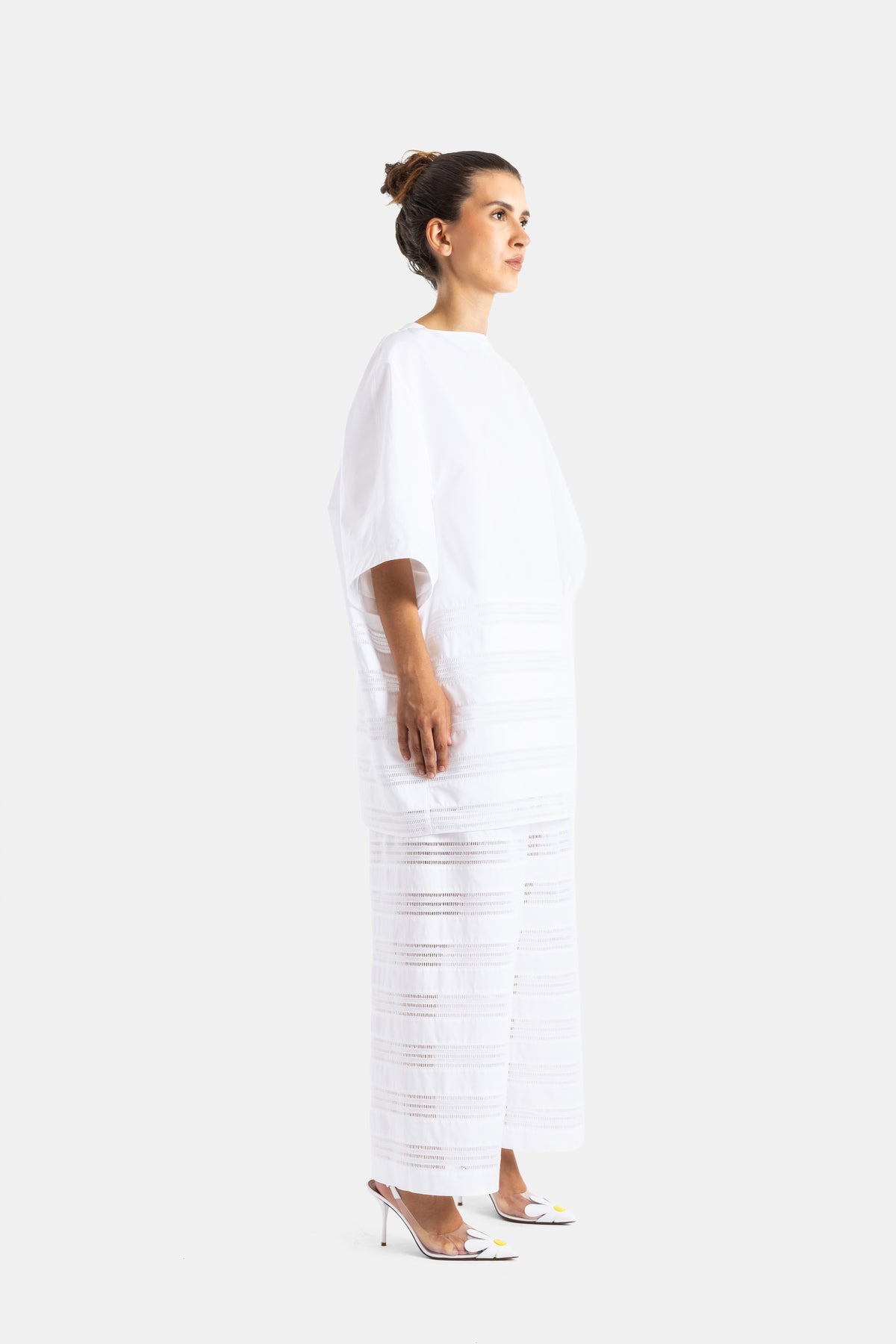 Maison Alaïa robe longue blanche en popeline vue de profil, bas ajouré semi-transparent et talons slingback