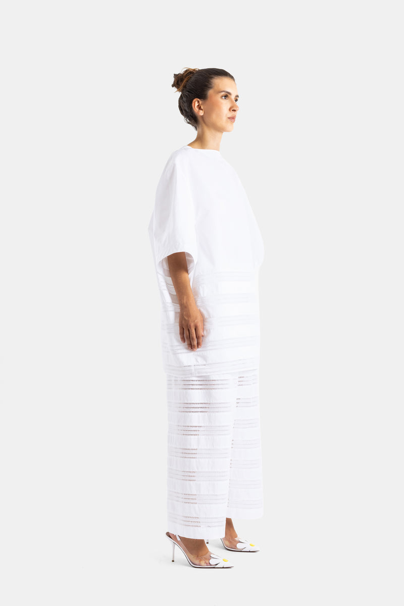 Maison Alaïa robe longue blanche en popeline vue de profil, bas ajouré semi-transparent et talons slingback
