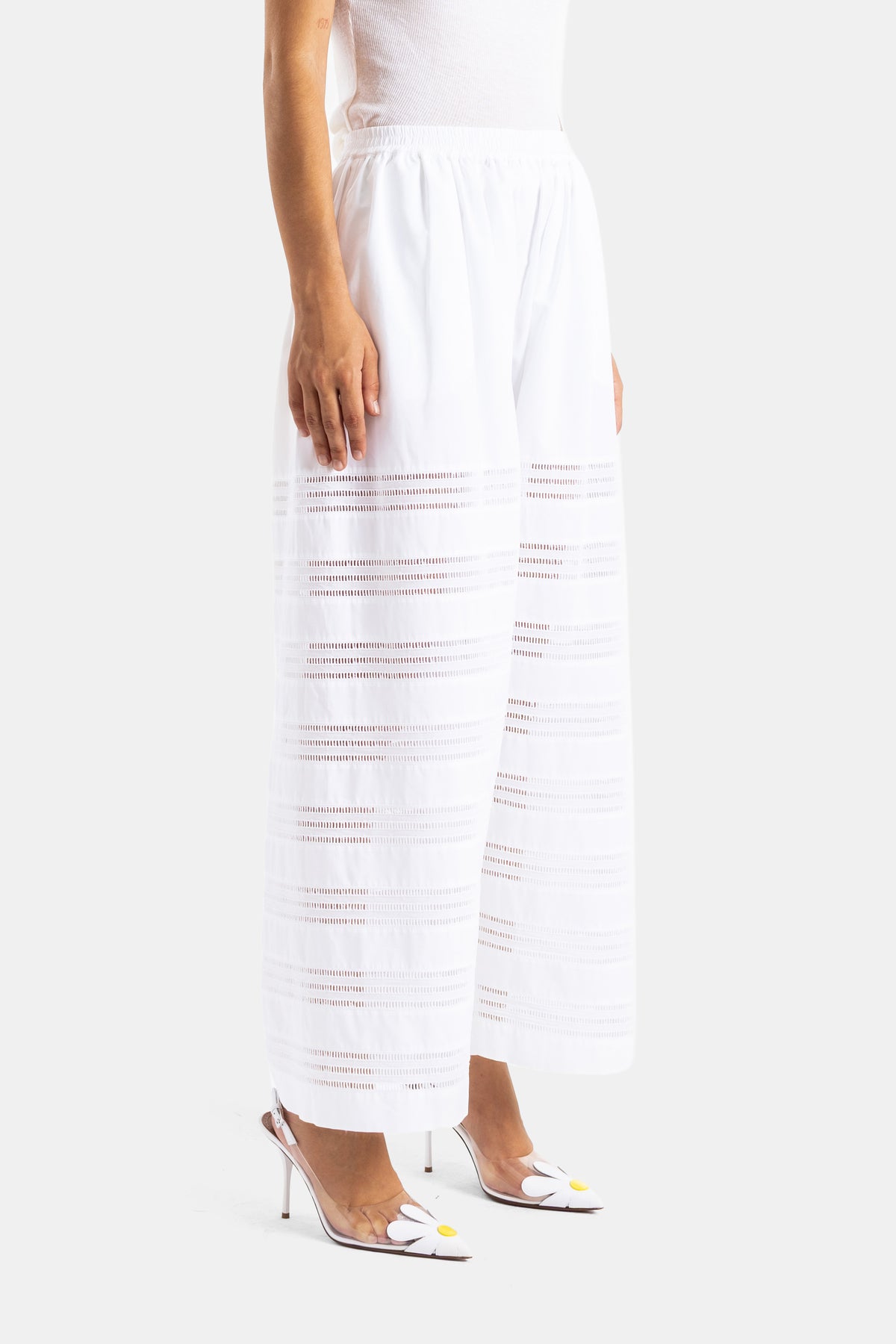 Maison Alaïa pantalon femme blanc vue de profil broderie ajourée rayures horizontales et escarpins fleurs