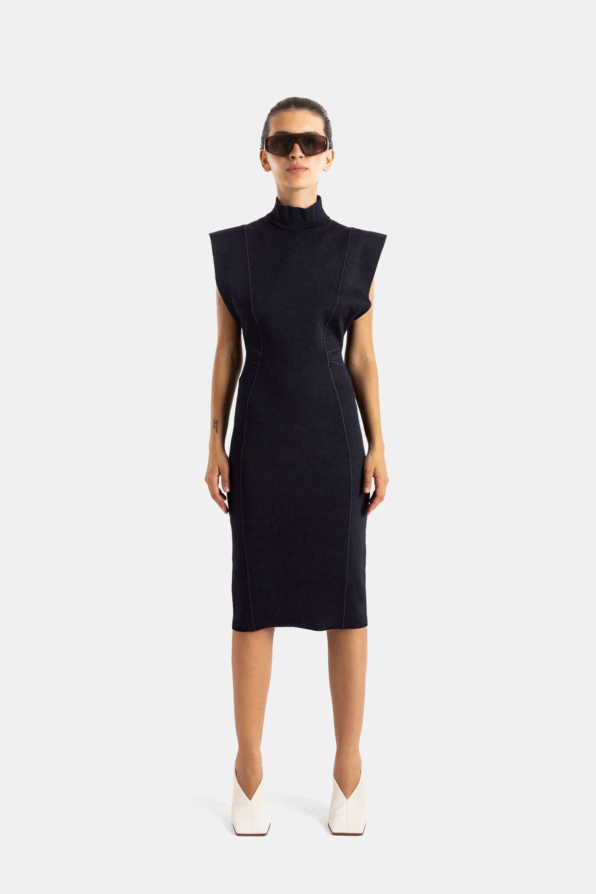 Maison Alaïa robe longue noire maille compacte vue frontale épaules carrées lunettes sport marron bottines blanches