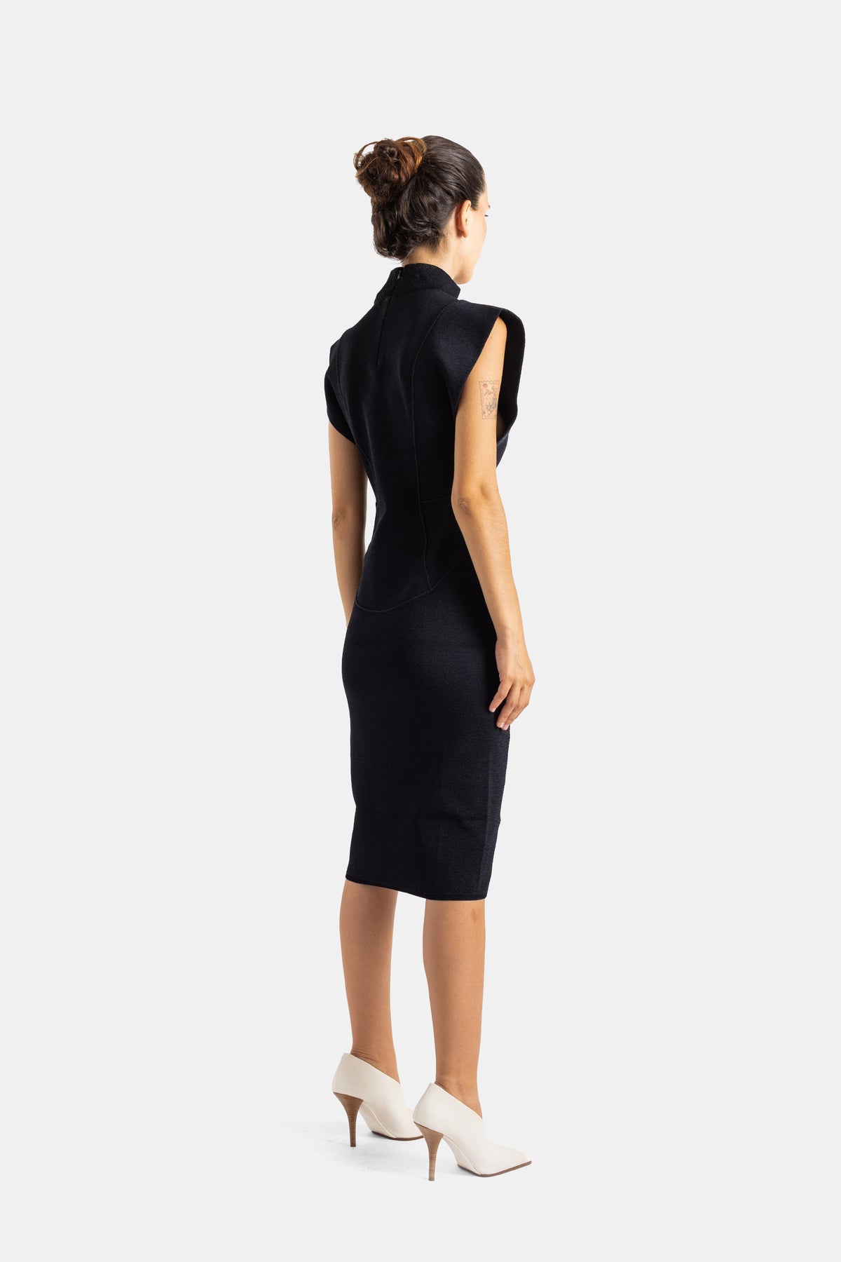 Maison Alaïa robe fourreau noire dos tatouage bras zip dorsal maille structurée mules blanches talon aiguille