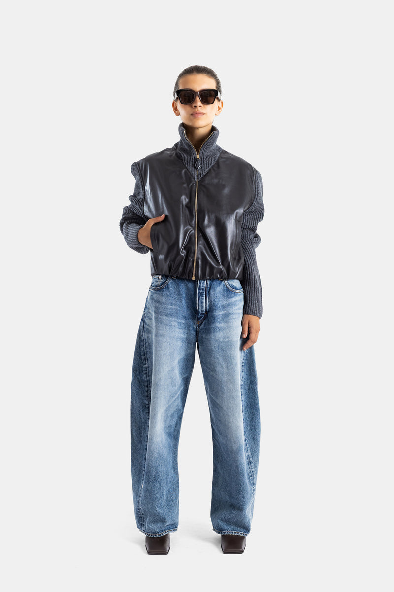 Maison Alaïa veste hybride femme portée de face, jean large bleu délavé, boots carrées noires, look streetwear luxe