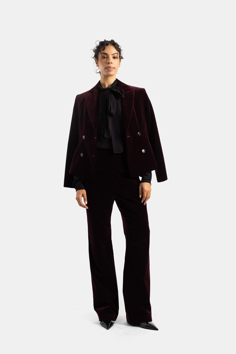 Blusa nera Maison Alaïa sotto completo in velluto bordeaux, lavallière annodata, total look elegante da donna.