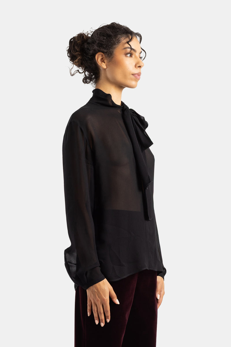 Maison Alaïa blouse noire semi-transparente vue de profil, cuffs boutonnés et ruban lavallière pendant