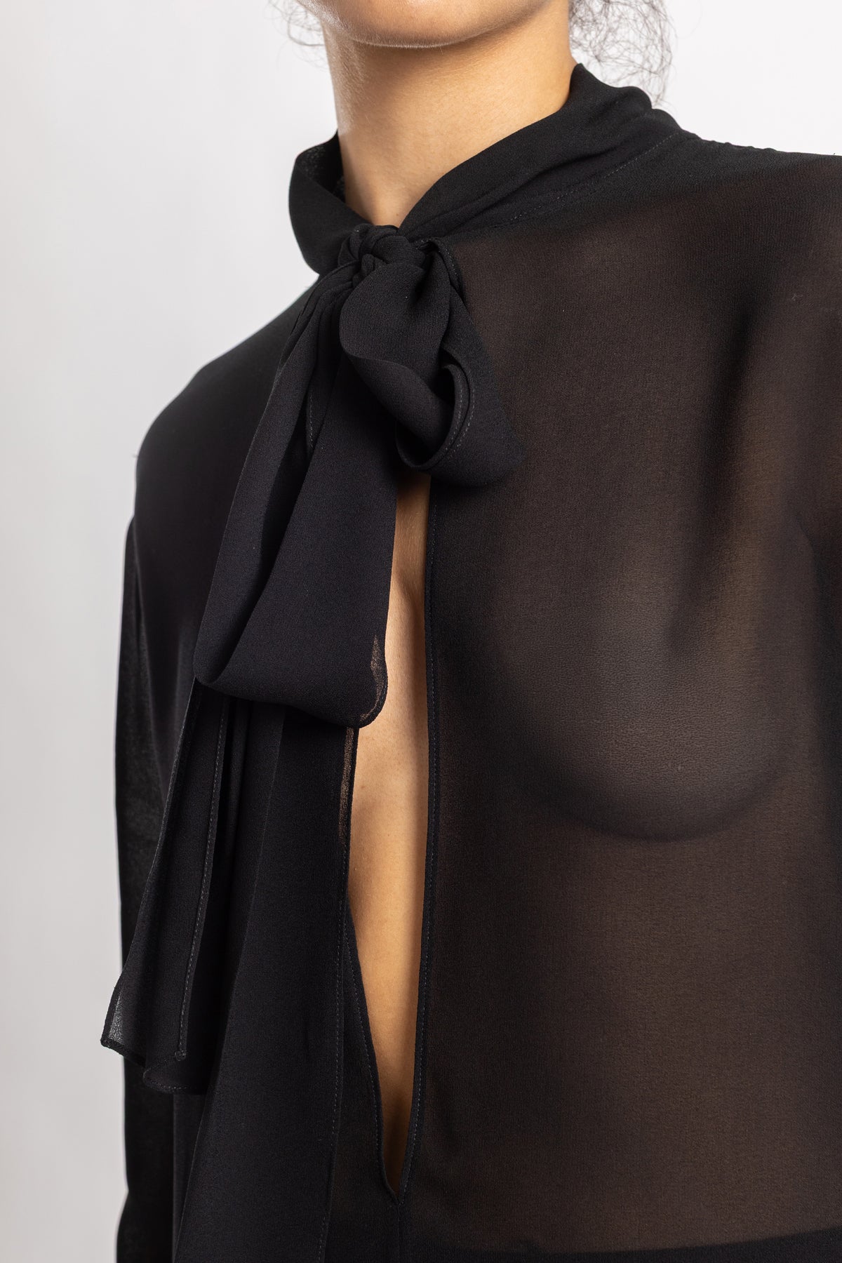 Maison Alaïa blouse chiffon noir transparente, décolleté plongeant et nœud lavallière gros plan vue frontale