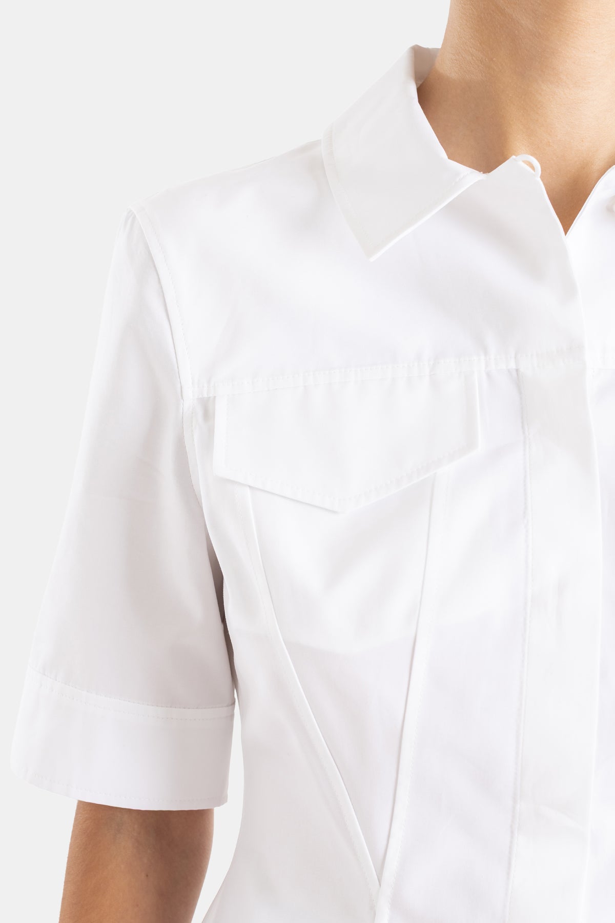 Maison Alaïa top coton blanc, encolure en V structurée et poche poitrine en biais, détail épaule