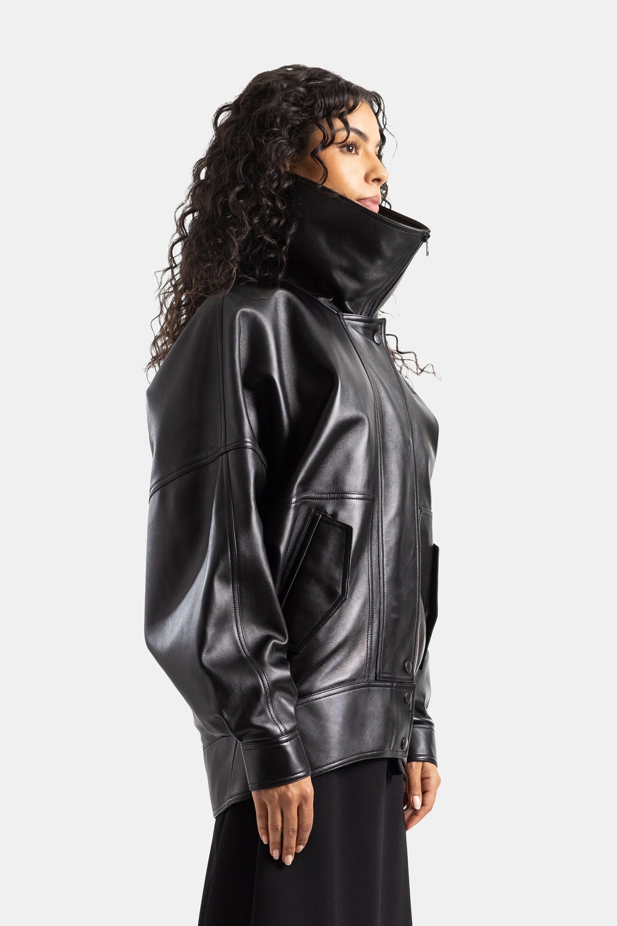 Giacca di pelle nera Balenciaga da donna, vista di profilo con tasca applicata, collo a lupetto e taglio oversize.