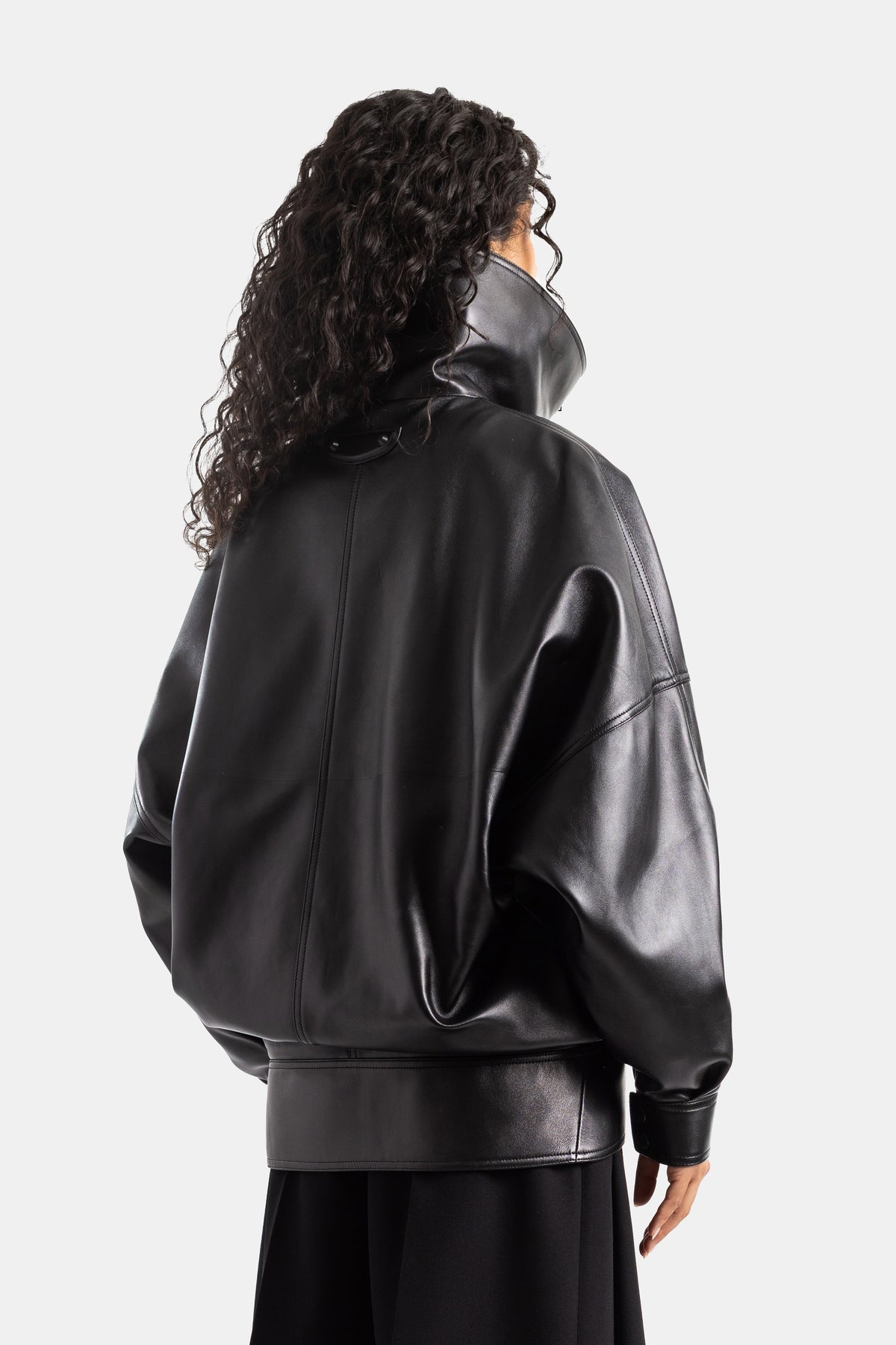 Giubbotto in pelle nera Balenciaga da donna, vista posteriore con cuciture a vista, collo a lupetto e capelli ricci.