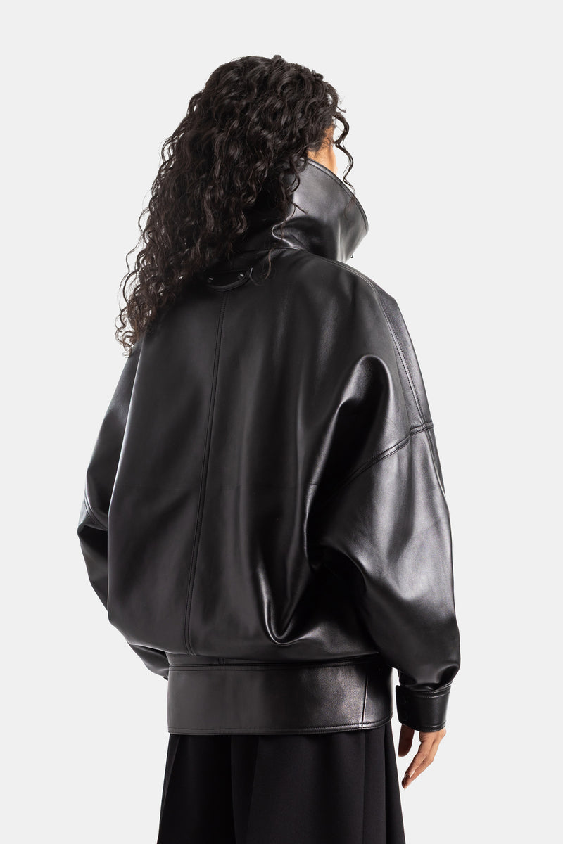 Giubbotto in pelle nera Balenciaga da donna, vista posteriore con cuciture a vista, collo a lupetto e capelli ricci.