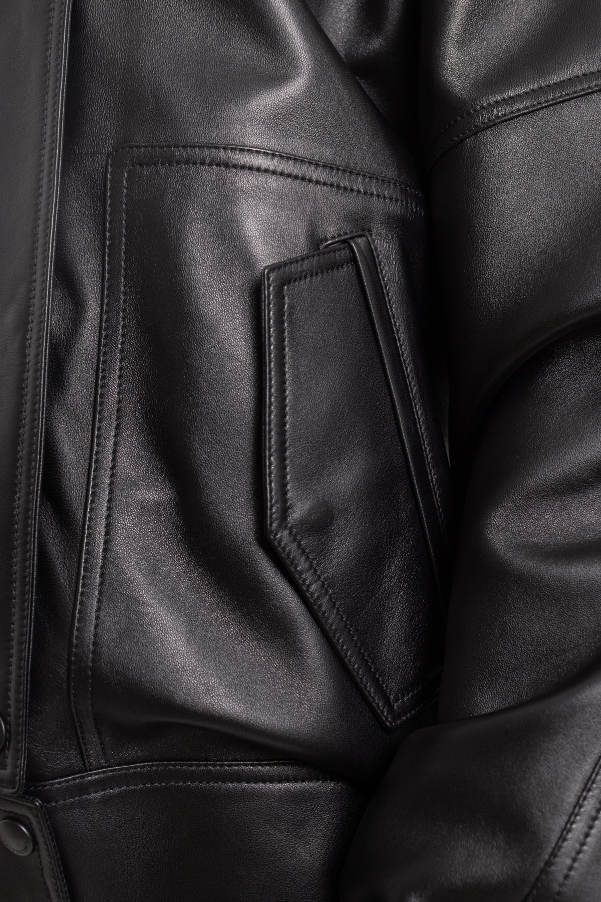 Dettaglio del giubbotto in pelle nera Balenciaga con tasca applicata asimmetrica, cuciture a vista e finitura liscia.