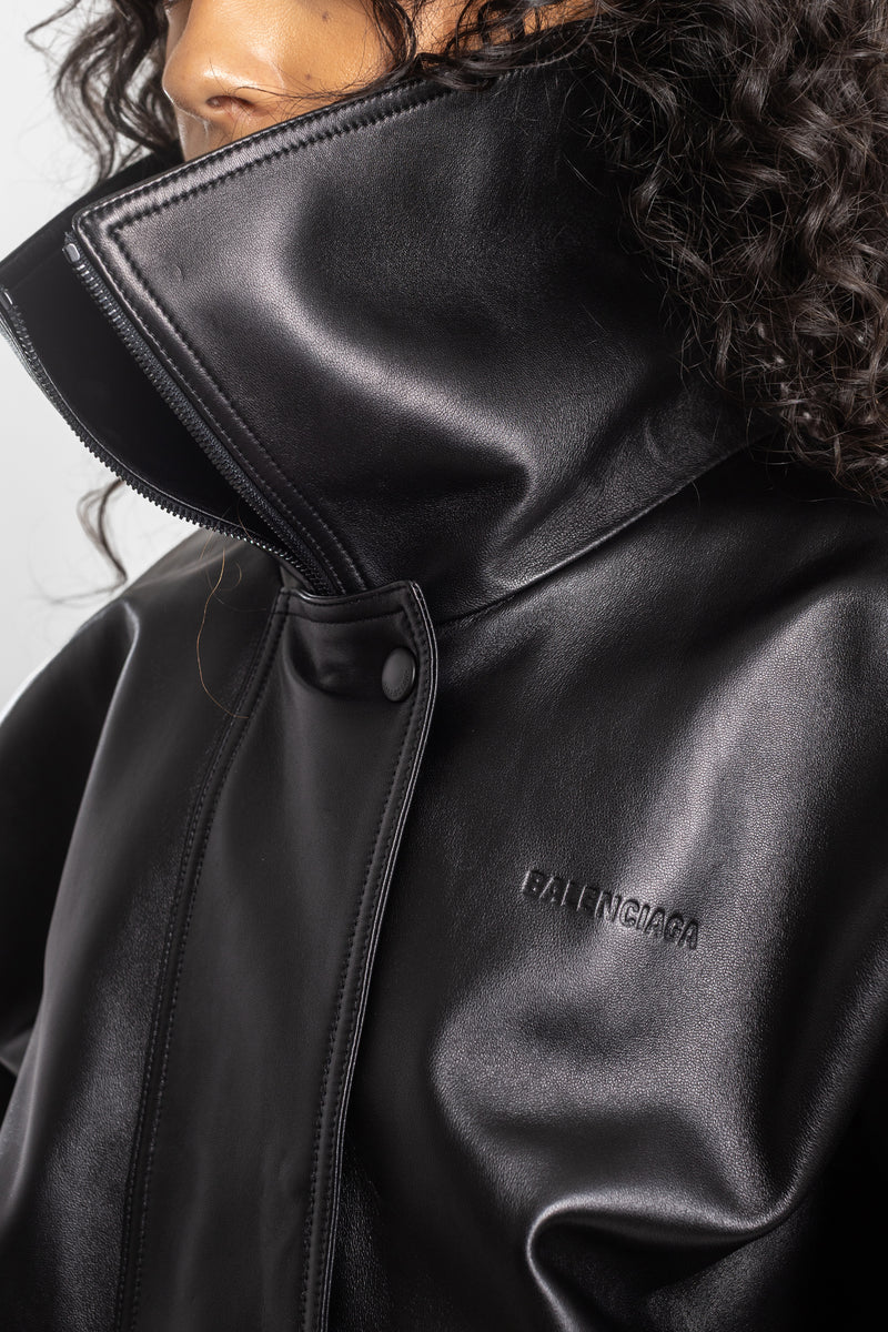 Primo piano del giubbotto in pelle nera Balenciaga da donna, con logo a rilievo, collo alto con zip e bottoni a pressione.