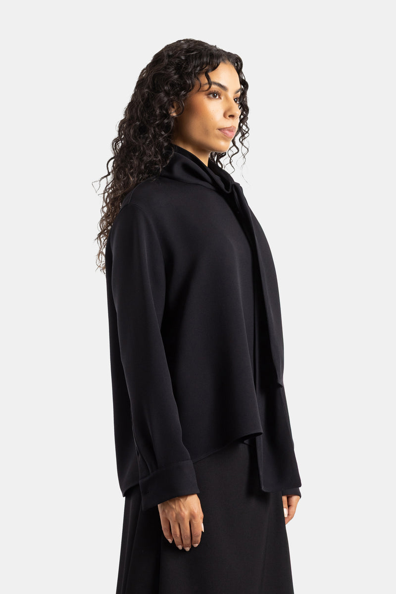 Blusa nera Balenciaga dal taglio strutturato vista di profilo con lavallière cadente e fondo svasato in crêpe.