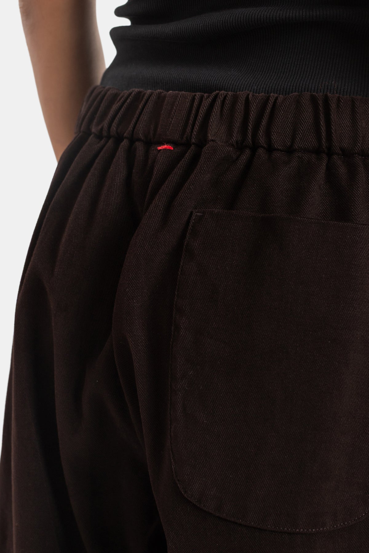 Zoom-out of Casey Casey Jog Ah dark brown corduroy trousers showing gathered waist and red stitch detail.