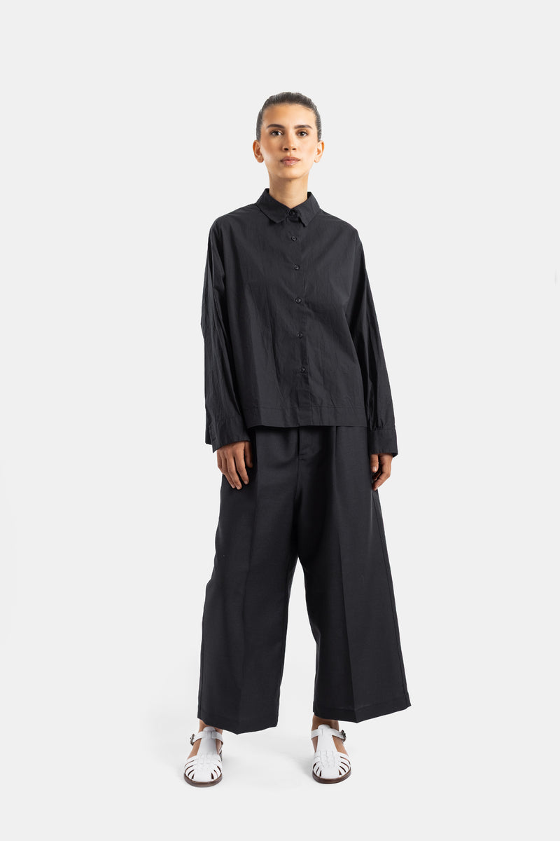Casey Casey chemise Biggy portée en total look noir avec pantalon large plissé et sandales blanches femme