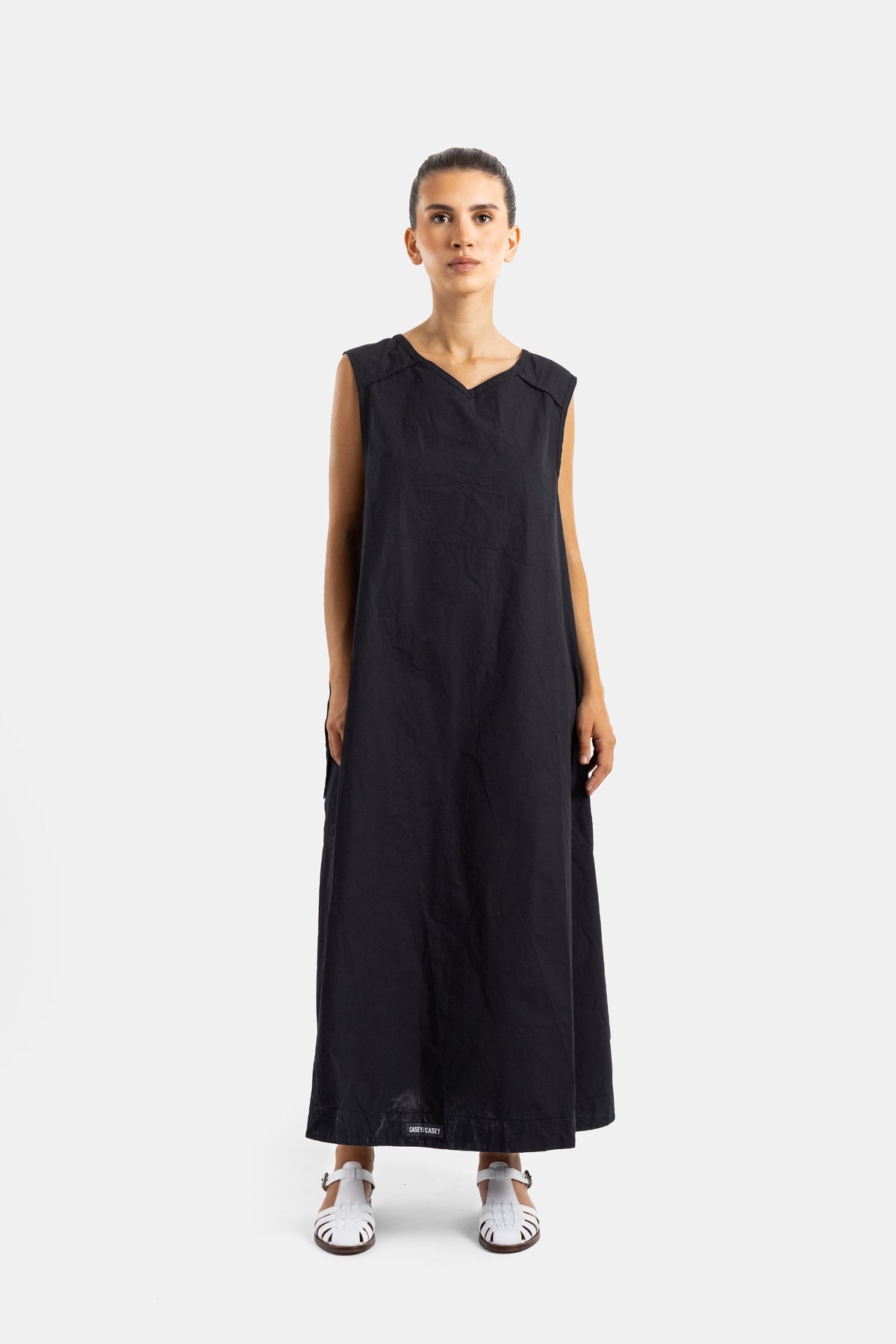 Casey Casey robe tablier maxi noire froissée col V structuré portée avec sandales blanches à brides, silhouette décontractée