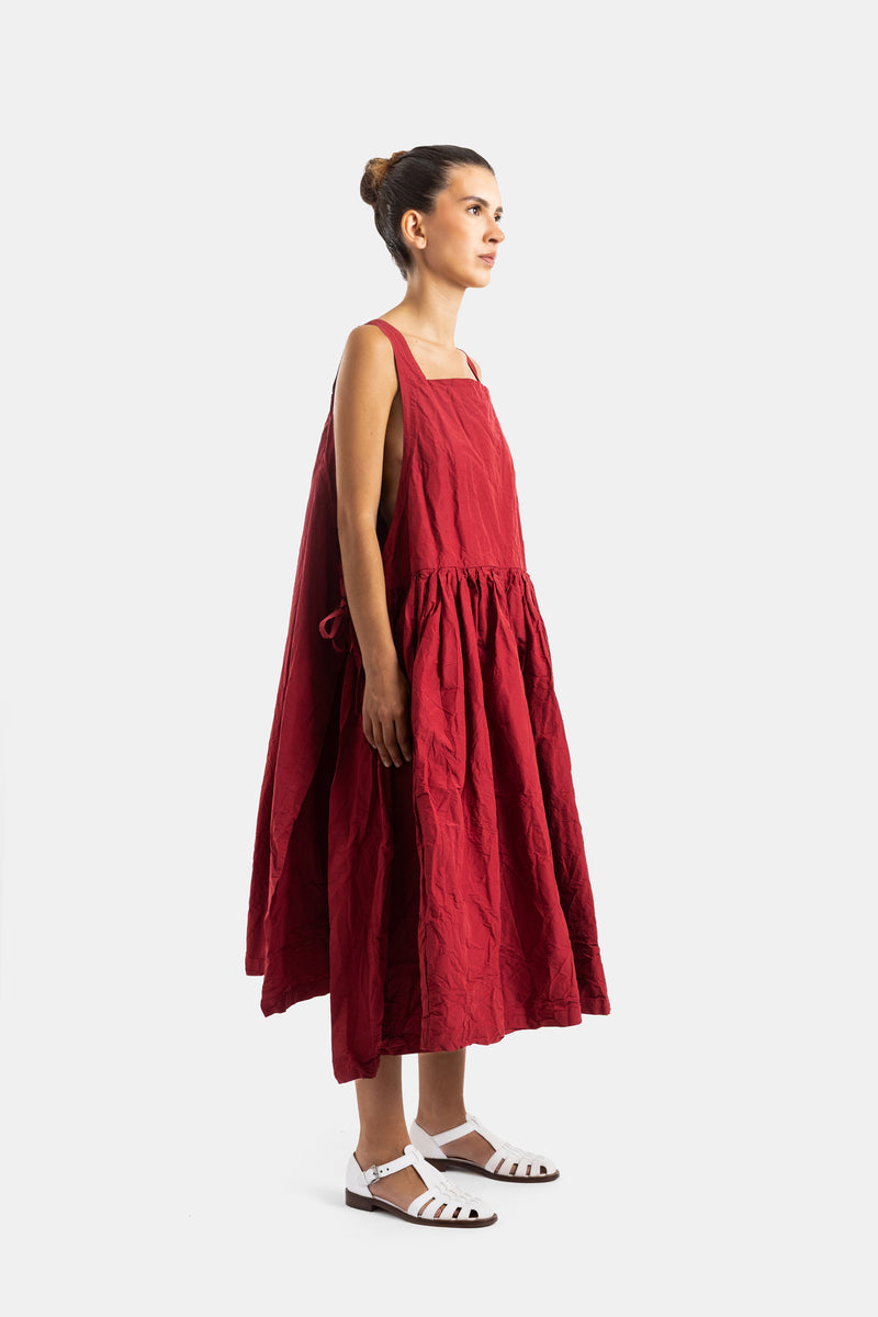 Casey Casey robe Nina rouge mi-longue vue de profil, jupe froncée volumineuse et sandales blanches
