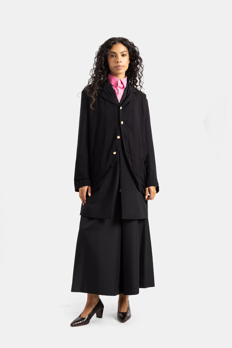 Casaco fluido Comme des Garçons preto silhueta vanguardista com camisa fúcsia gola franzida e saia palazzo