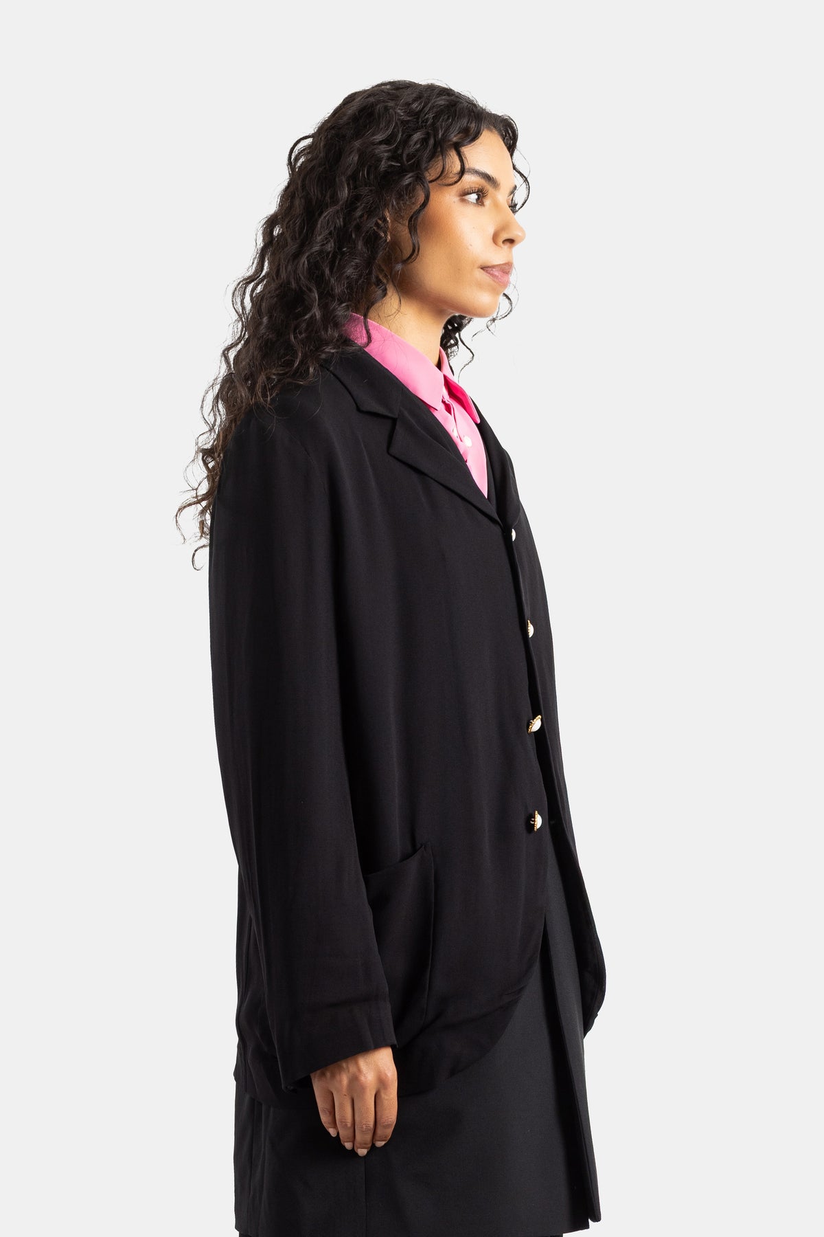 Blazer comprido Comme des Garçons preto de perfil sobre camisa cor-de-rosa fúcsia com botões dourados nacarados