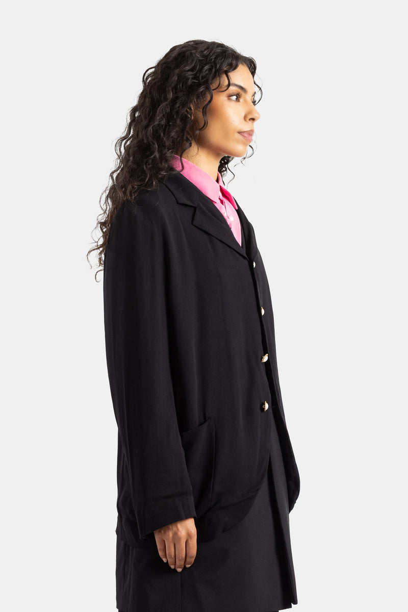 Blazer comprido Comme des Garçons preto de perfil sobre camisa cor-de-rosa fúcsia com botões dourados nacarados