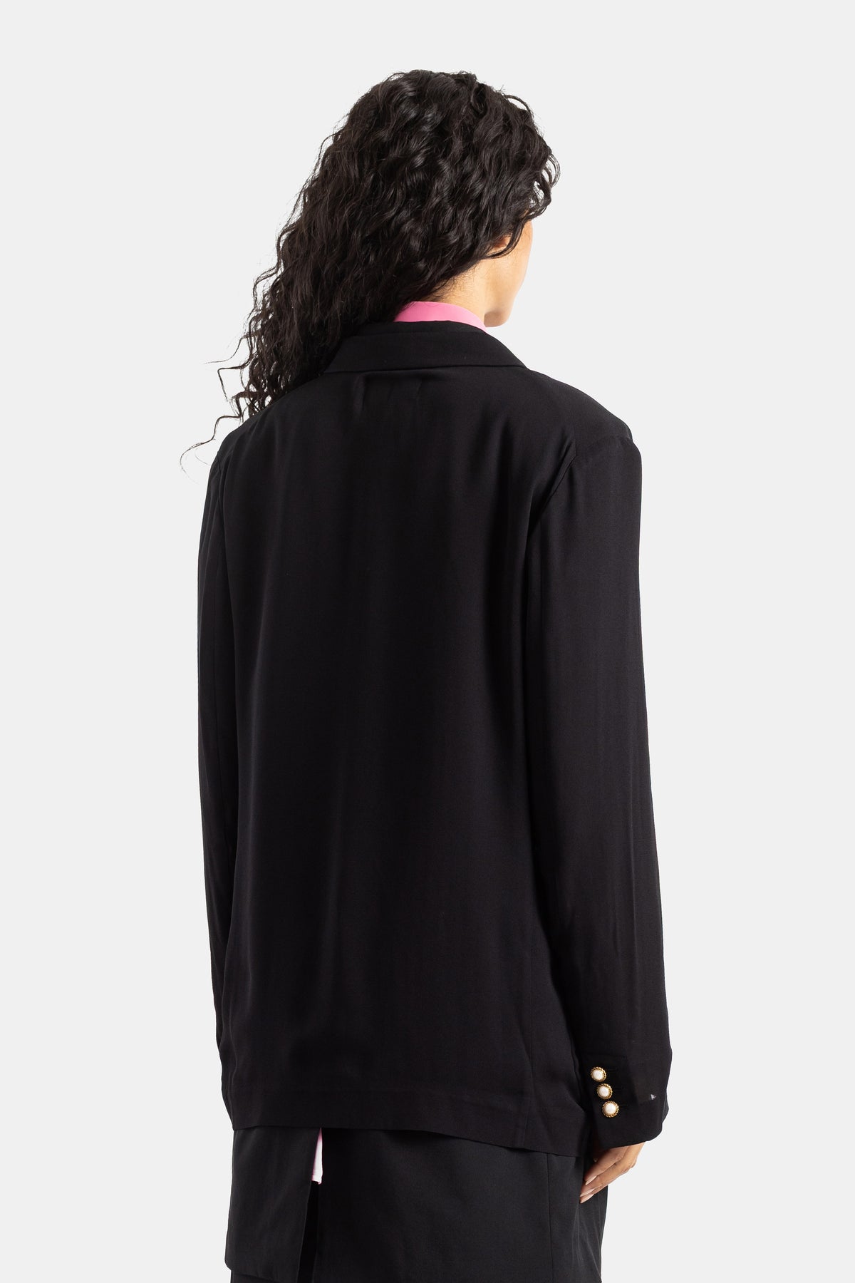 Casaco Comme des Garçons preto fluido visto de costas cabelo encaracolado botões dourados nacarados no punho