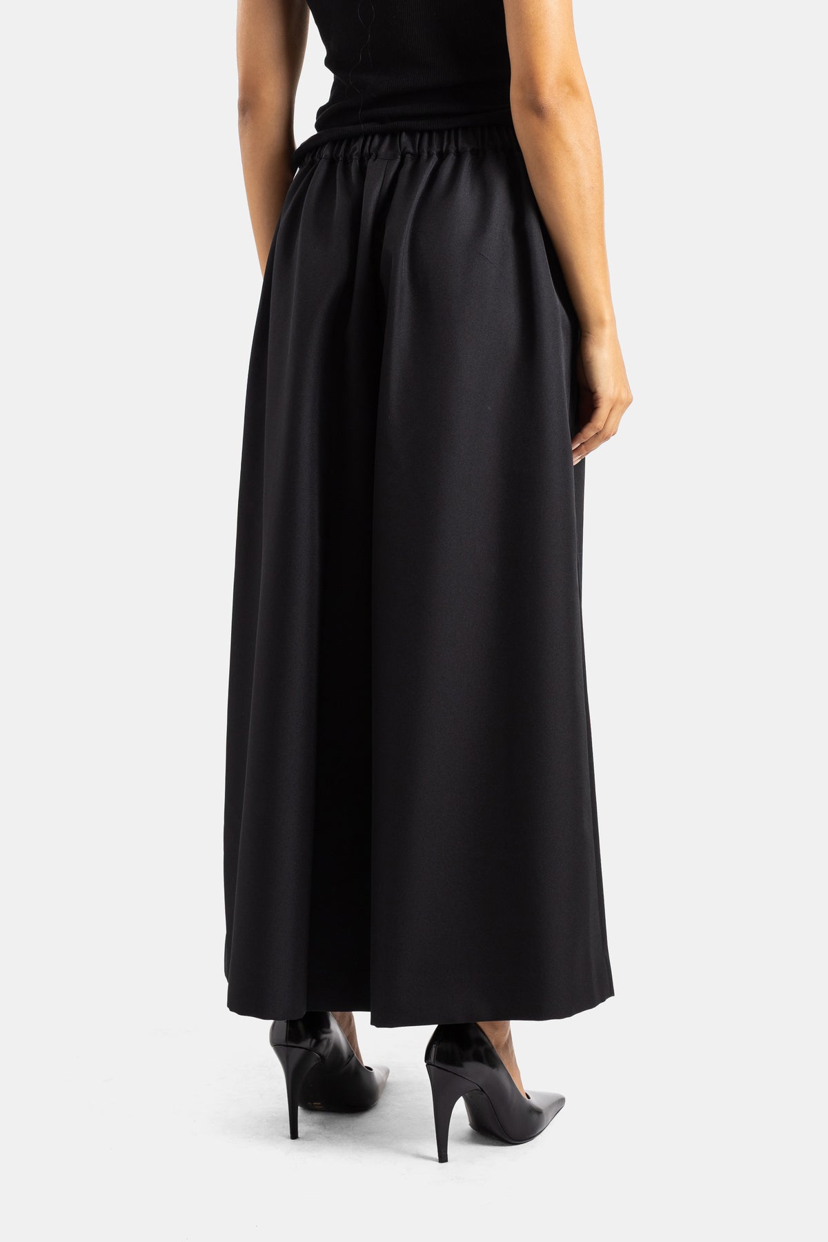 Rückansicht der weiten schwarzen Comme des Garçons Hose mit elastischem Bund und spitzen Lack-Pumps.