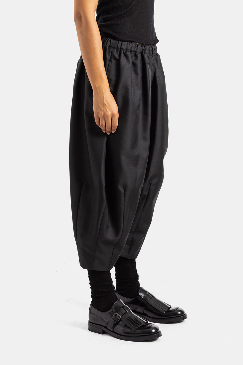 Comme des Garçons sarouel corto negro de perfil, corte globo estructurado con leggings y mocasines