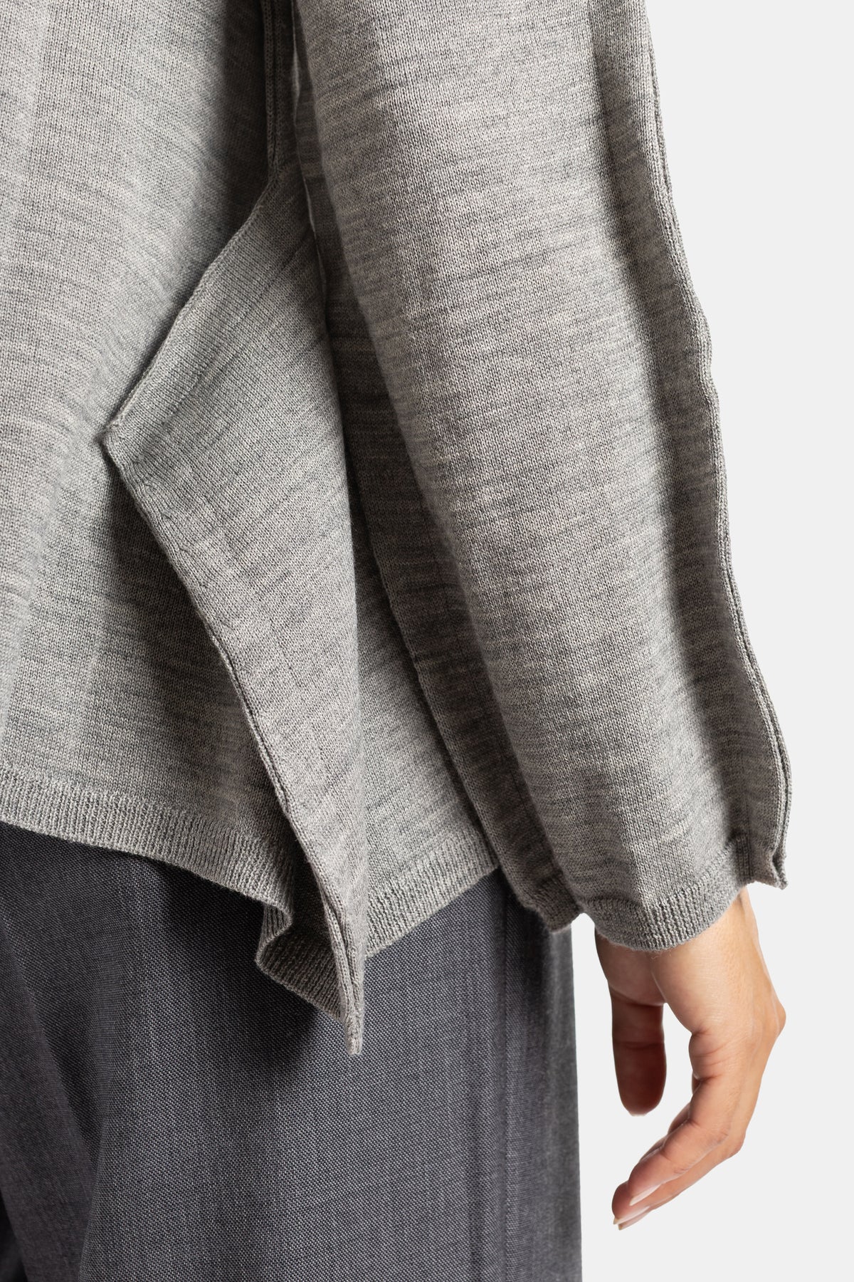 Detalle del puño de canalé y bajo asimétrico fluido del jersey de lana gris Comme des Garçons para mujer