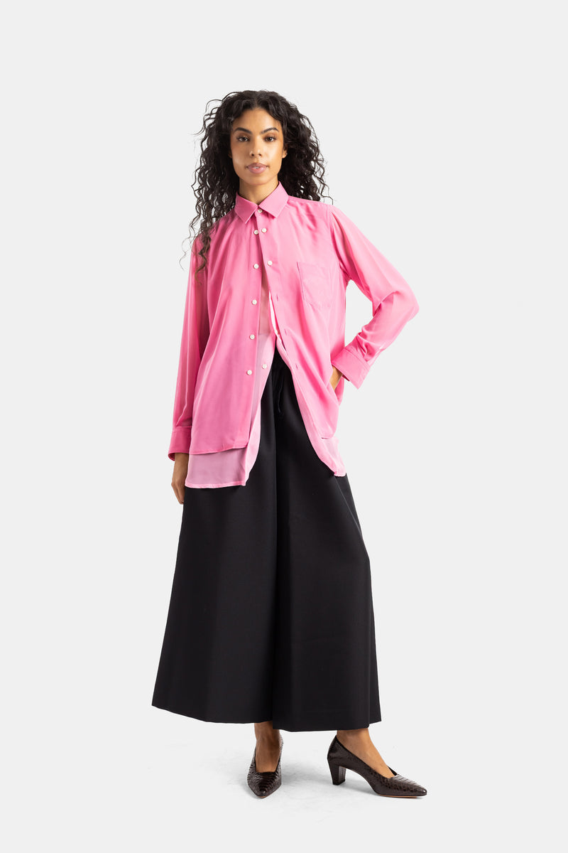 Fließendes Comme des Garçons Hemd in Rosa, elegant kombiniert mit einer weiten schwarzen Hose und braunen Pumps.