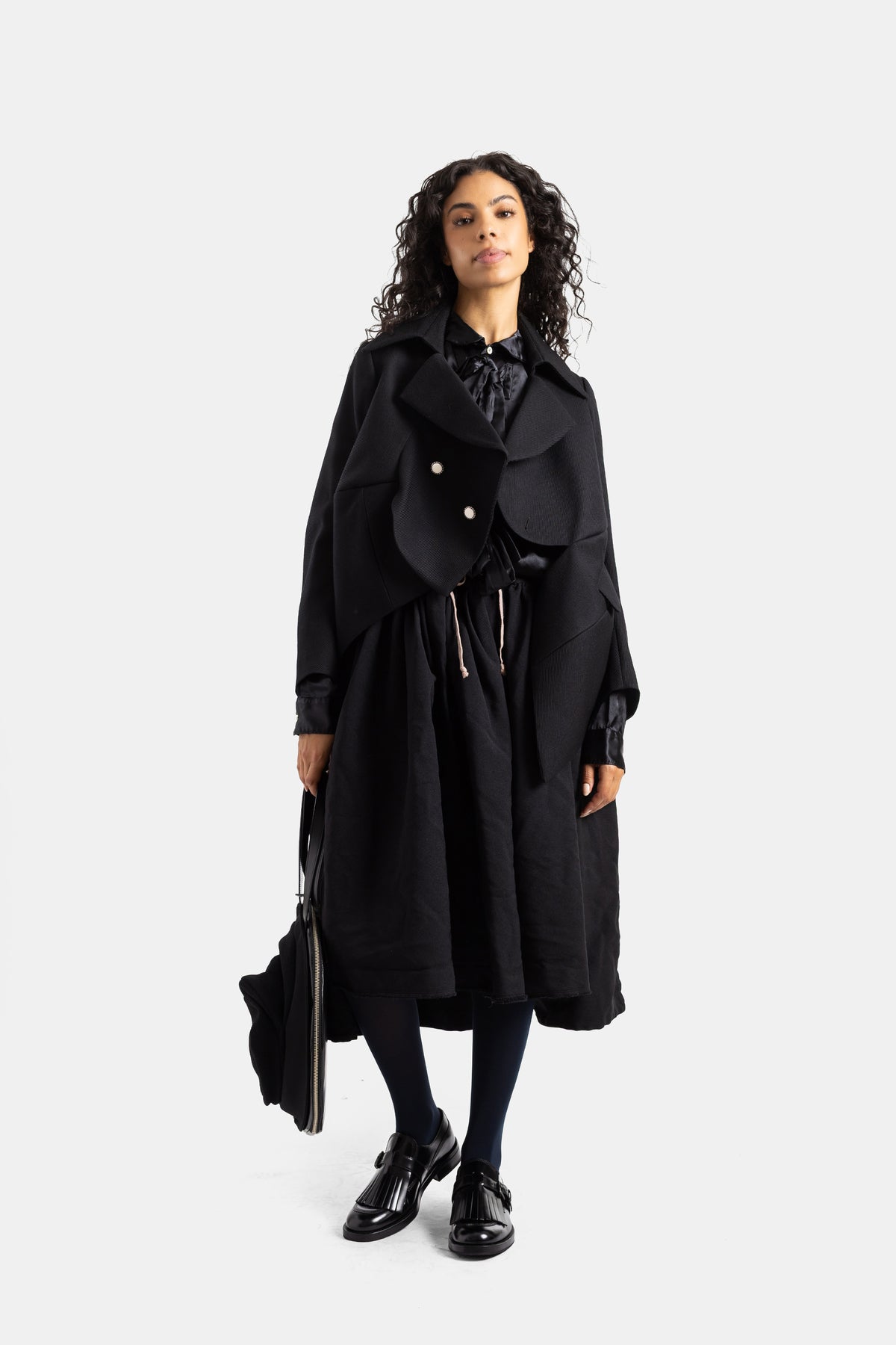 Falda voluminosa negra Comme des Garçons con abrigo oversize y mocasines de charol en un look total black.