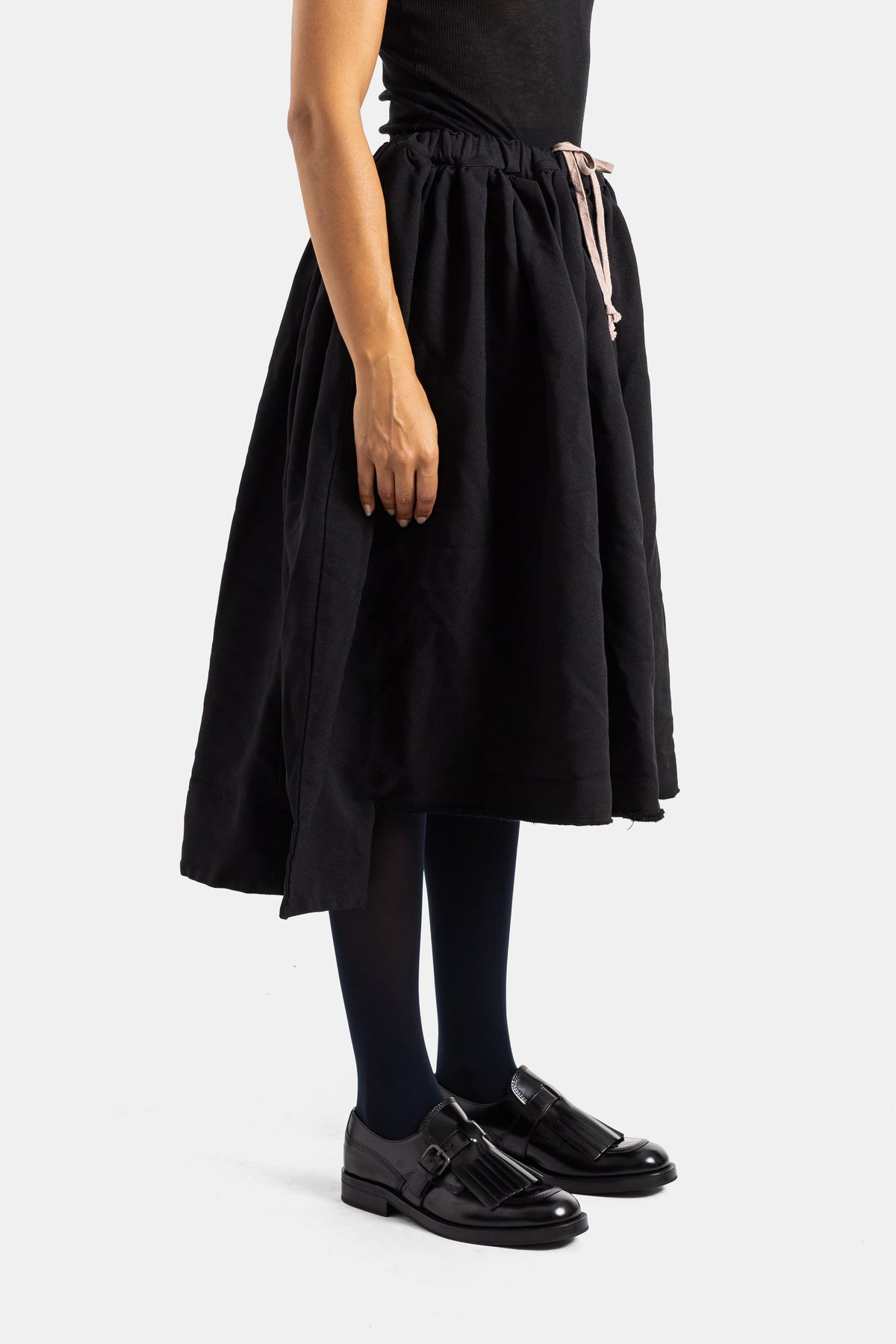 Falda midi negra fruncida Comme des Garçons con cintura elástica y lazo satinado rosa pálido, vista lateral.