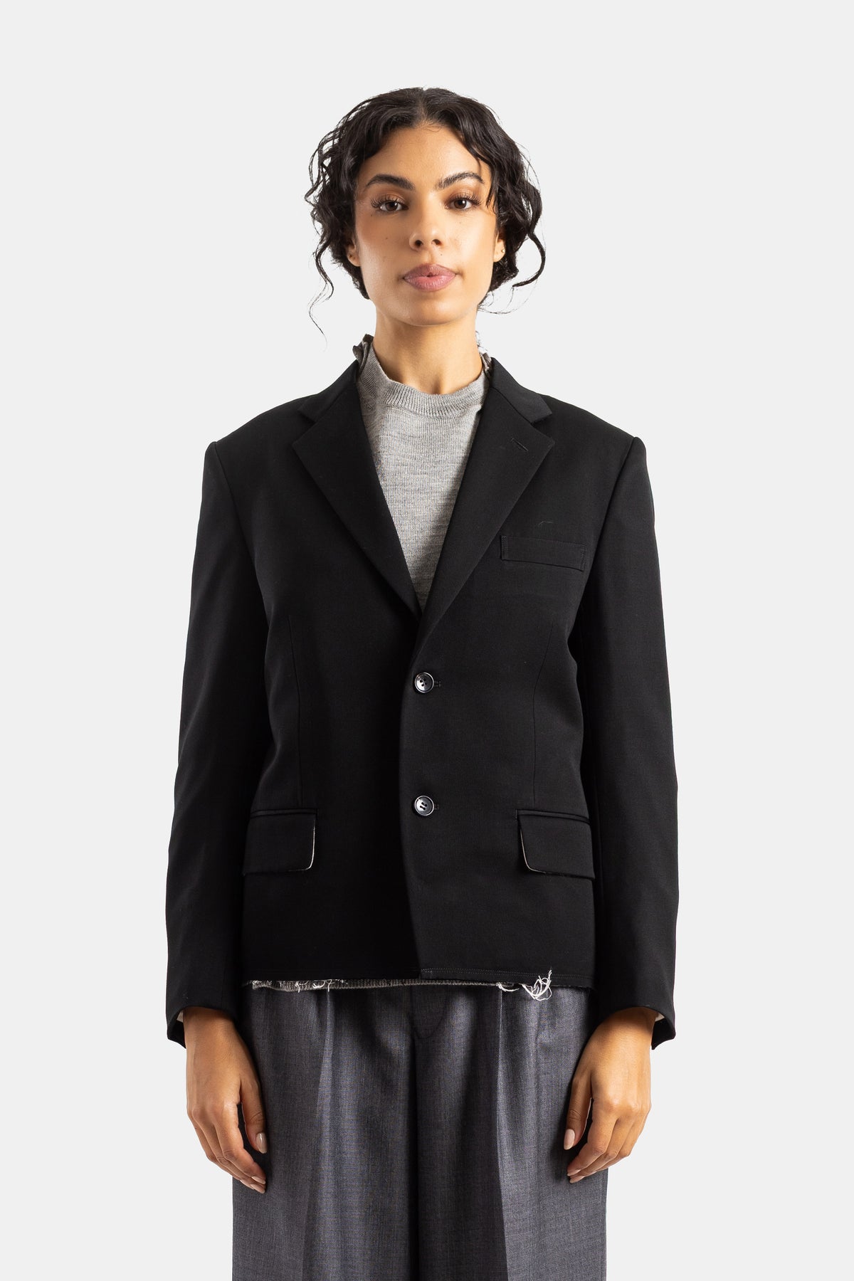 Chaqueta sastre oversize Comme des Garçons en lana negra, cuello de muesca, dos botones y bajo deshilachado.