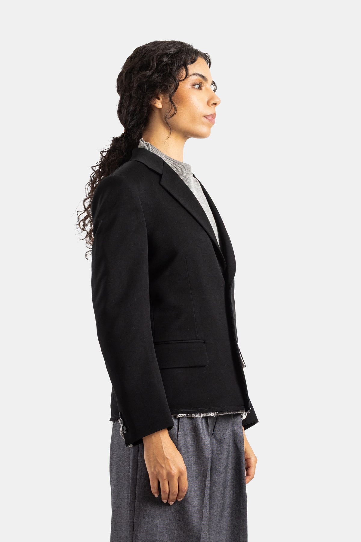 Blazer de mujer Comme des Garçons de lana negra de perfil, con dobladillo deshilachado y corte corto estructurado.