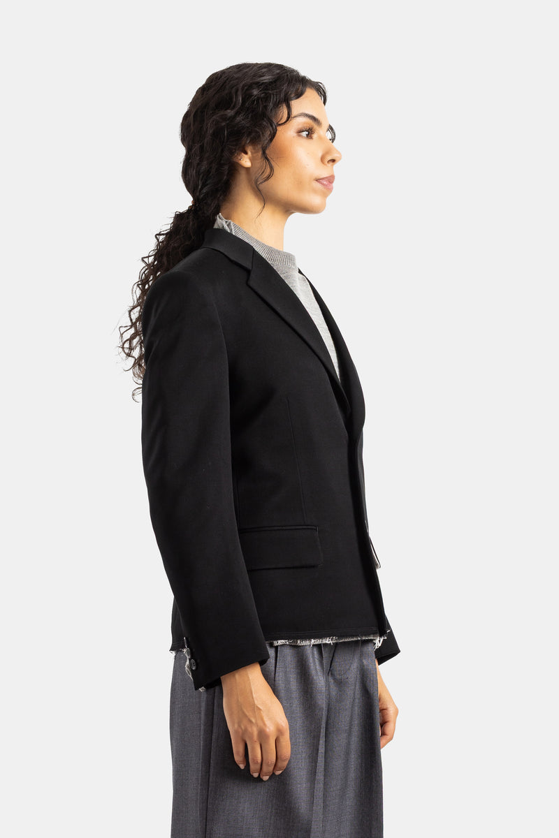 Blazer de mujer Comme des Garçons de lana negra de perfil, con dobladillo deshilachado y corte corto estructurado.