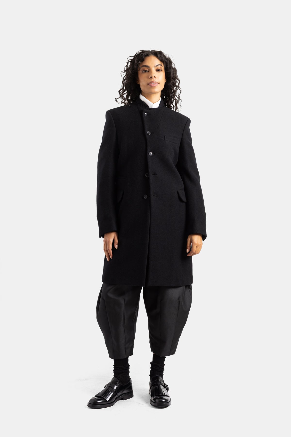 Abrigo Comme des Garçons de lana negra para mujer con hombros estructurados, bolsillos de solapa y look negro.