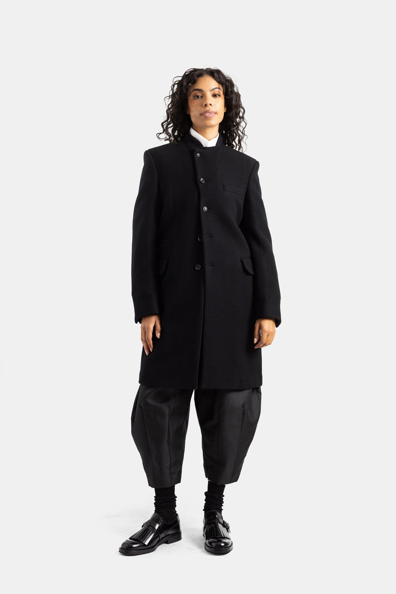 Abrigo Comme des Garçons de lana negra para mujer con hombros estructurados, bolsillos de solapa y look negro.