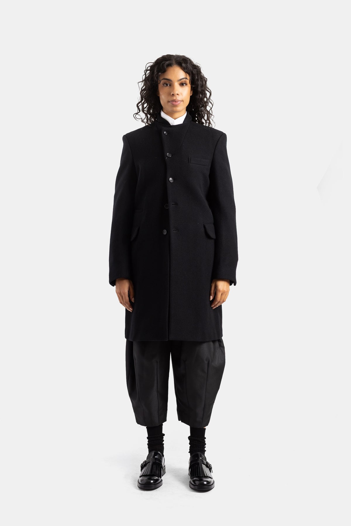 Abrigo midi Comme des Garçons de lana negra con cuello alto asimétrico y un corte recto muy estructurado.