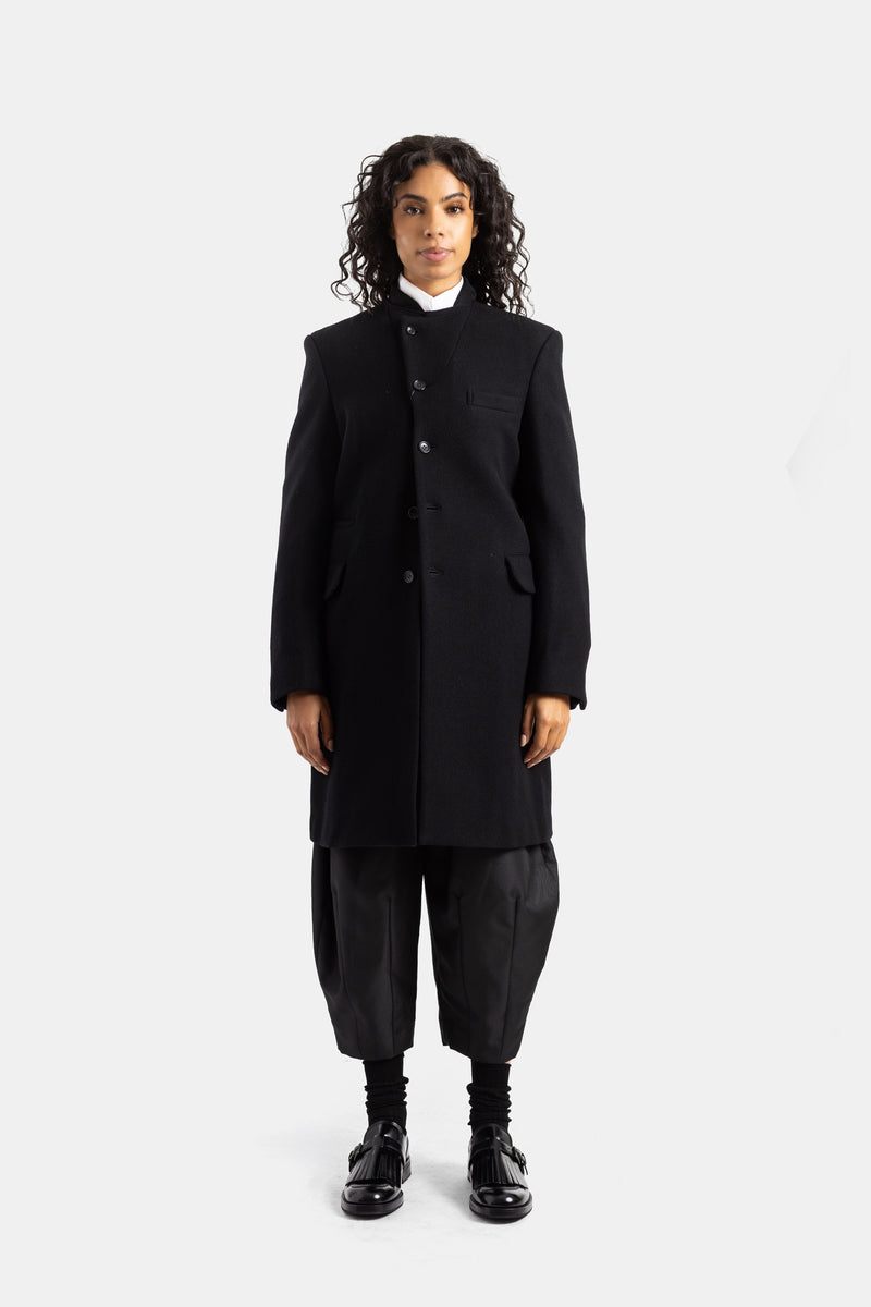 Abrigo midi Comme des Garçons de lana negra con cuello alto asimétrico y un corte recto muy estructurado.